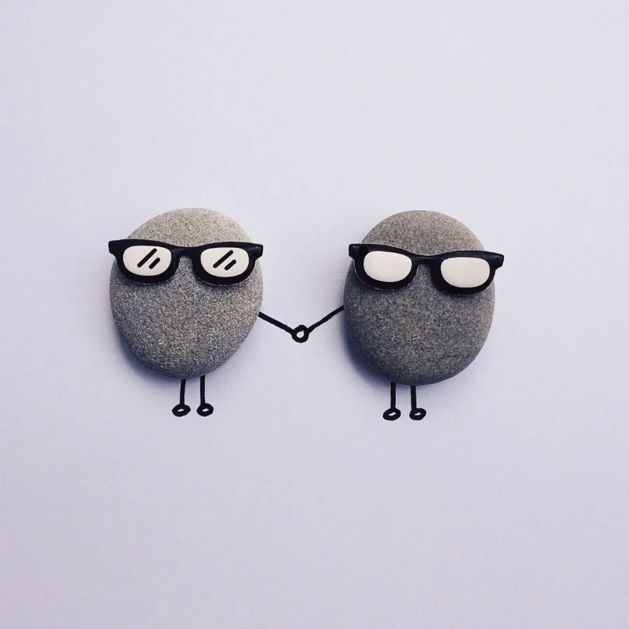 two-pebbles-with-glasses-holding-hands-on-a-white-surface